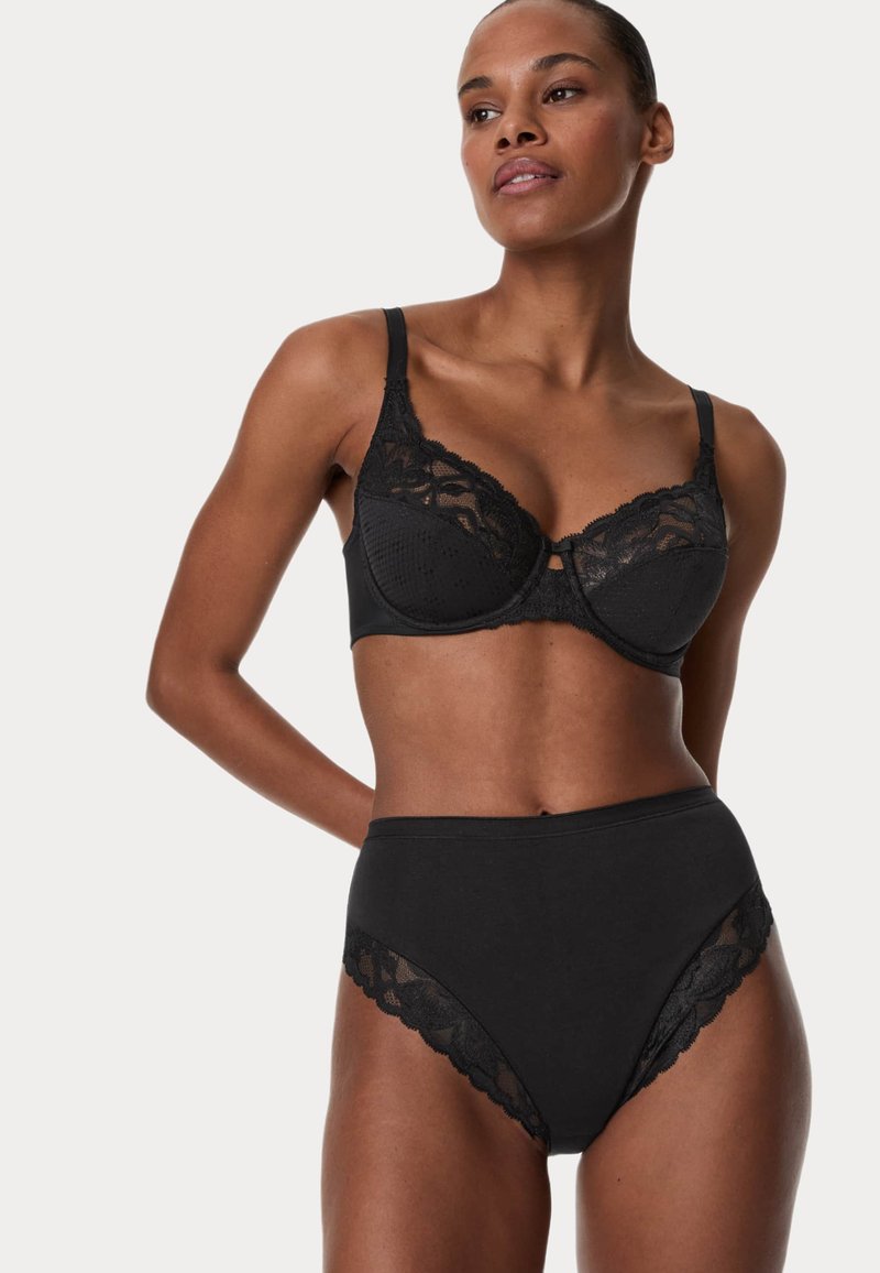 Svart lingerie-set som inkluderar en behå med texturerade kupor och spetskanter, kombinerat med högmidjade trosor som har spetsdetaljer på sidorna.