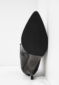 Scarpa nera in pelle con tacco alto, punta affilata e tacco a stiletto sottile. La suola è liscia e presenta un logo in rilievo discreto.