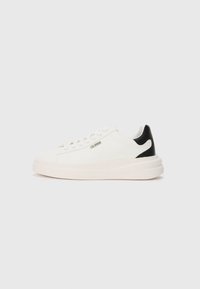 Hvite sneakers med en teksturert stoffoverdel, svart hælakkent, flate snøring og tykk hvit såle. Har et metallisk logo på siden.