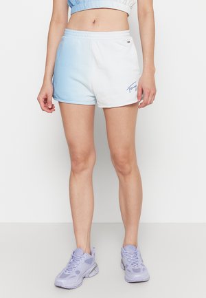 Pantalones cortos en degradado blanco y azul claro con cinturilla elástica y detalle del logo azul en la parte frontal, combinados con zapatillas deportivas lavanda.