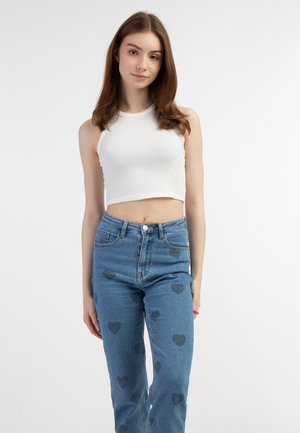 Witte geribbelde crop top met mouwloos ontwerp, gecombineerd met blauwe high-waisted jeans met hartvormige patronen in donkerder blauw.