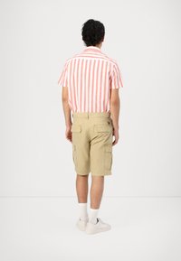 Camicia a maniche corte con righe verticali rosse e bianche abbinata a pantaloni cargo beige, dotati di tasche e di un taglio rilassato. Sneakers bianche completano l'outfit.