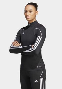 Top sportivo nero con colletto a zip parziale, caratterizzato da strisce bianche lungo le maniche e un pannello testurizzato sulle spalle.