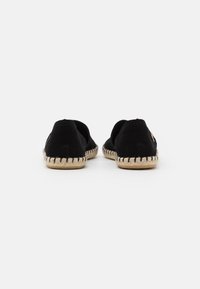 Espadrilles de tela negra con suela de yute trenzado y costuras negras. Diseño sin cierre con talón abierto y puntera redondeada. Silueta simple y clásica.