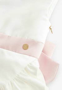Baltas satīna kleita ar maiga rozā jostu un krokotu detaļu, akcentēta ar zeltītu apaļu logotipu. Gluda tekstūra, eleganta dizaina.