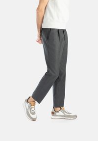 Szare plisowane spodnie o dopasowanym kroju, zestawione z szaro-białymi sneakersami z brązowymi akcentami i teksturowanymi nakładkami.