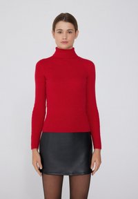 Czerwony sweter typu golf wykroju dopasowanego, wykonany z dzianiny, z długimi rękawami, w zestawie z czarną skórzaną mini spódnicą. Gładka tekstura, minimalne detale.