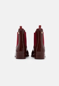Botas de tobillo de charol burdeos con paneles laterales elásticos, tacón curvado y acentos de tela en contraste en el cuello.