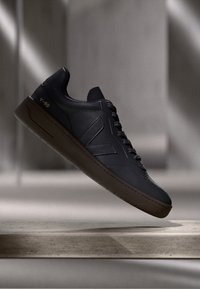 Svarte lærersneakers med rund tå, flat gummisåle og en fremtredende side-logo. Har snøring og gullfiner.