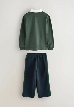 Dunkelgrünes Langarmoberteil mit einem weißen Kragen, kombiniert mit marineblauen Jogginghosen mit grünen Seitenstreifen. Weicher Stoff, lockere Passform.