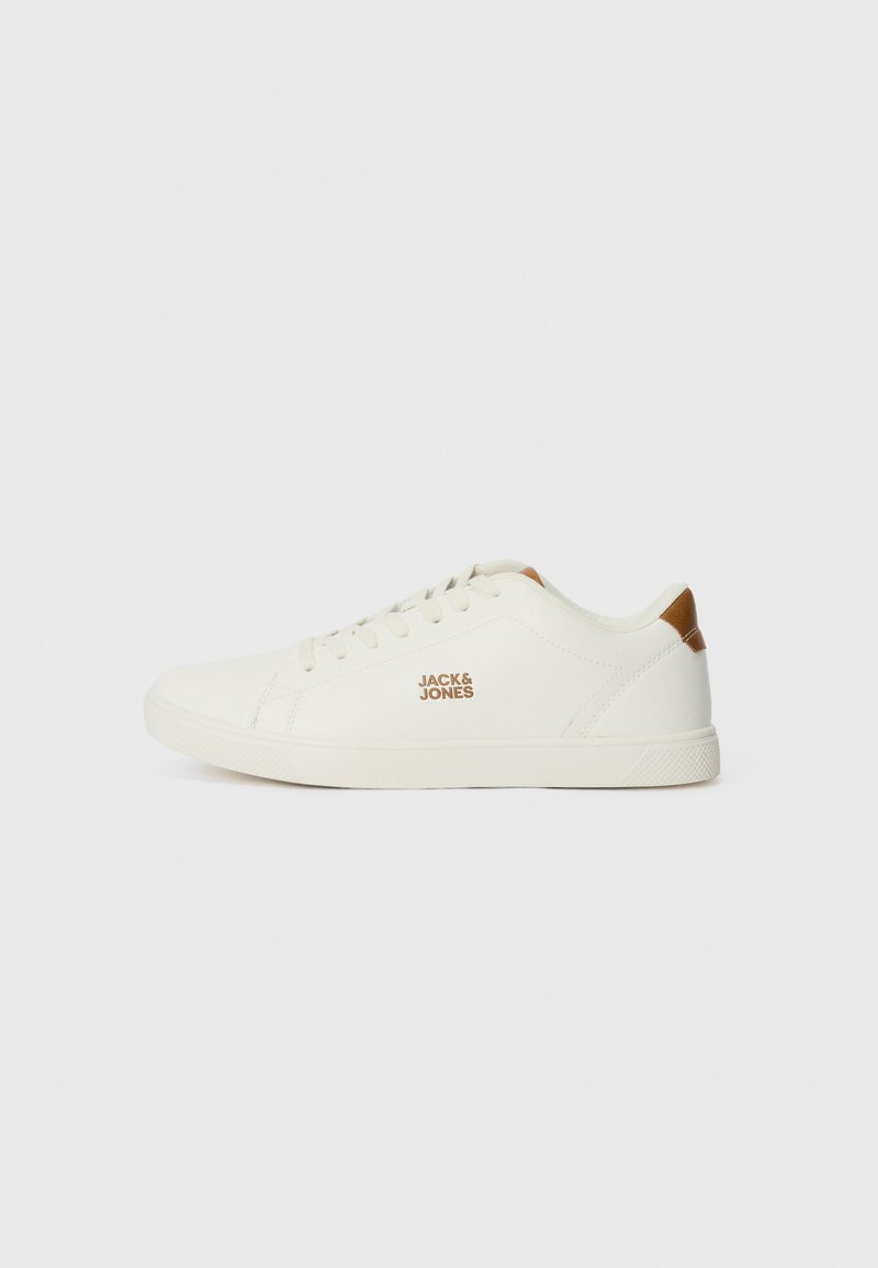 Zapatillas de lona blancas con una suela texturizada, que presentan un logo dorado en el lateral y un acento marrón en el talón. Diseño de cordones, puntera redondeada.