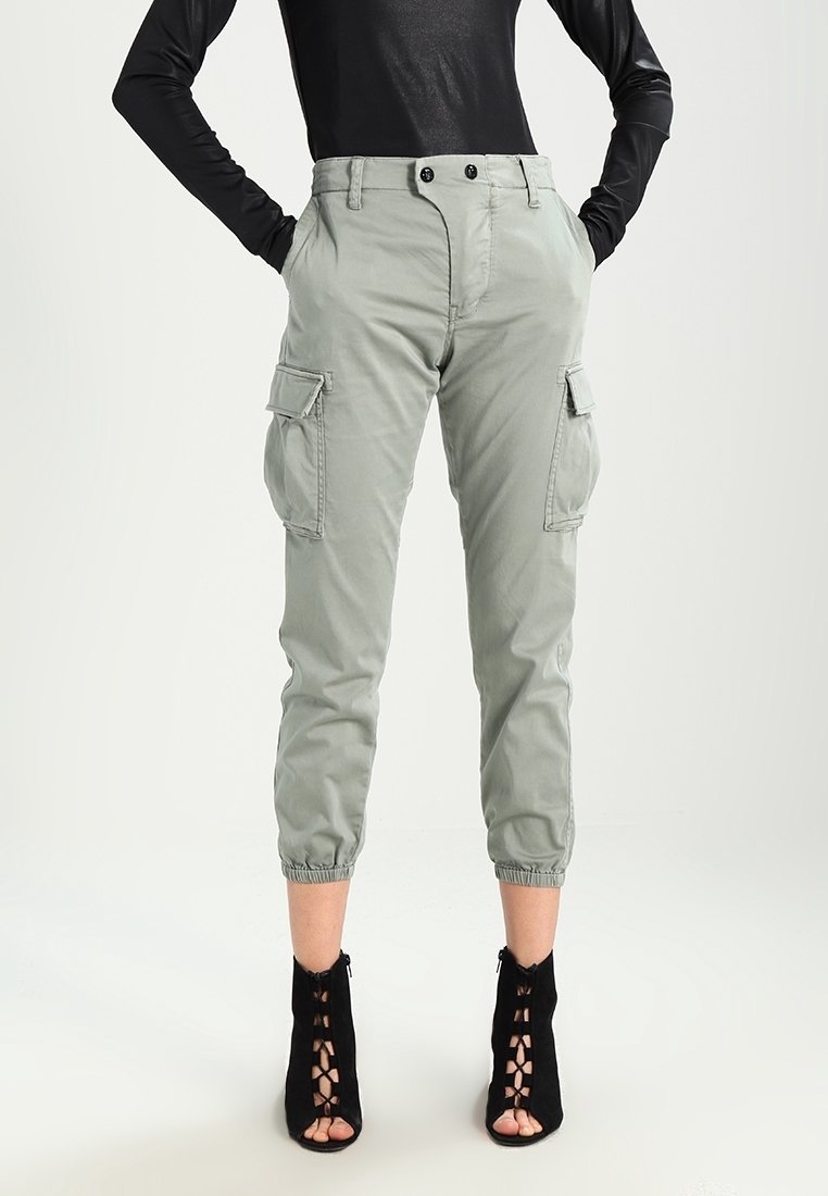 Lichtgrijze cargobroek met elastische boorden en twee zijzakken. Gestyled met een getailleerde zwarte top en zwarte veterschoenen met hak.