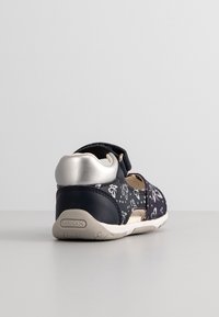 Chaussure enfant bleu marine avec motifs papillons blancs, talon argenté, bride réglable, et semelle beige avec le logo "GEOX".