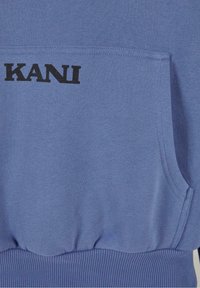 Tissu bleu avec une poche avant de type poche kangourou et le texte noir "KANI" imprimé près du bord supérieur de la poche.