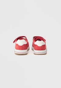 Red suede shoes with white fabric accents and Velcro straps, featuring a rounded heel and textured outsole for grip.