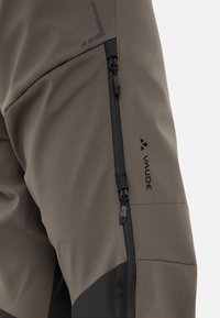 Taille-hoge buitenbroeken in gedempt olijfgroen, voorzien van een zijrits en zwarte accenten. Het materiaal lijkt duurzaam met een gladde textuur en logo's.