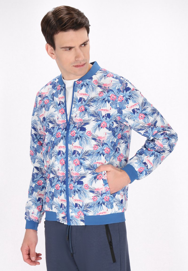 Giacca bomber floreale con stampa tropicale blu e rosa, materiale leggero, polsini e colletto a coste, e tasche laterali. Chiusura con zip sul davanti.