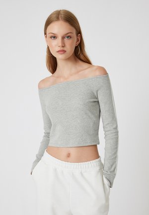 Top gris de manga larga sin hombros, diseño recortado, textura ajustada, con acentos laterales blancos, combinado con pantalones blancos de cintura elástica.