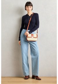 Námornícky pruhovaný top s dlhým rukávom, svetlo modré široké džínsy a hnedé podpätkové čižmy. Malá crossbody taška má textúrovaný krémový povrch a hnedé akcenty.