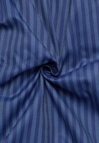 Marineblauwe stof met een gestructureerde weving, versierd met afwisselend dunne en dikke verticale strepen in lichtere blauwtinten.