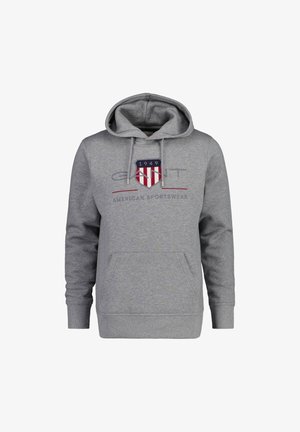 Sudadera gris con bolsillo canguro, capucha con cordón y un logo que presenta un escudo con rayas rojas y azules y texto. Material de mezcla de algodón.