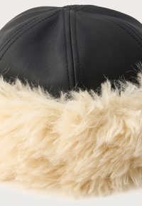 Black leather cap featuring a beige, fluffy faux fur trim along the base, showcasing a smooth texture and rounded design with stitched seams.