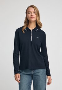 Granatowa koszulka polo z długim rękawem, z kołnierzykiem zapinanym na guziki, różowym wykończeniem i logo na piersiach. Miękka bawełniana tkanina, luźny krój.