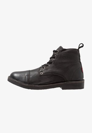 Bottes de cheville en cuir noir avec un bout rond, un design à lacets et une languette à l'arrière. Comprend des œillets en métal et une surface texturée.