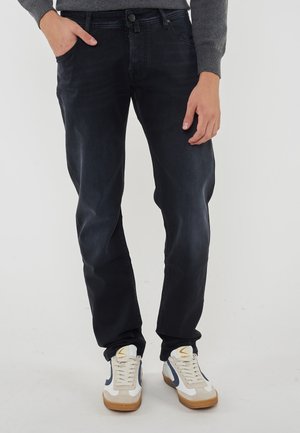 Donkerblauwe denim jeans met een rechte pasvorm, voorzien van een klassieke vijf-vaksontwerp en een gladde textuur. In combinatie met witte en marineblauwe sneakers.