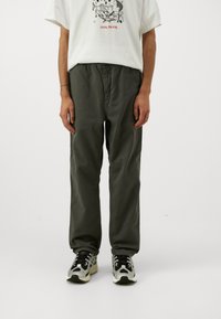 Olijfgroene katoenen broek met een relaxte pasvorm, voorzien van een elastische tailleband en zijzakken, gecombineerd met zwart-witte sportschoenen.