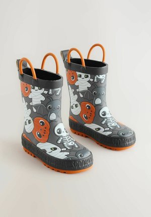 Graue Gummiregenstiefel mit Halloween-Motiv, die Geister, Kürbisse und Mumien zeigen. Mit orangen Akzenten und doppelten Griffen für ein einfaches An- und Ausziehen.