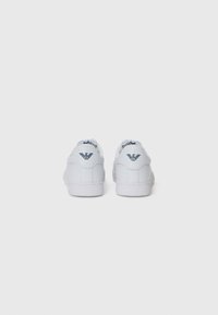 Adidași albi dintr-un material sintetic neted, cu un design low-top, având un detaliu cu logo și o talpă din cauciuc pentru aderență.