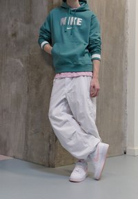 Nike turkos hoodie med vitt märke, över en rosa skjorta, kombinerad med vida vita byxor och vita sneakers med rosa detaljer.