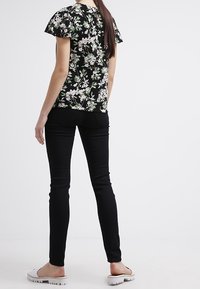 Top negro con estampado floral y mangas cortas con volantes, combinado con pantalones negros ajustados y calzado claro. Tejido suave y diseño ajustado.