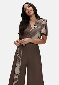 Brown wrap dress with short sleeves, featuring a patterned sash in beige and brown tones. Soft fabric and fluid design for a relaxed fit.