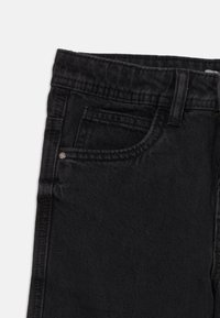 Close-up van zwarte denim jeans die de tailleband, de riemlus, het voorvak en het muntvak met metalen klinknagel tonen, op een witte achtergrond.