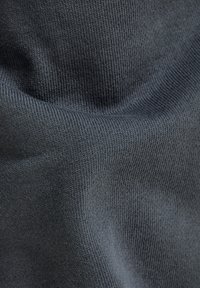 Tejido de punto de color gris oscuro que muestra una superficie texturizada con finos ribetes, de apariencia suave y ligeramente estirado en algunas áreas.