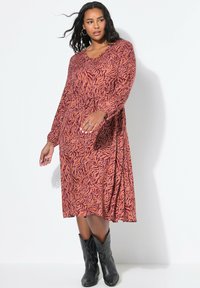 Robe à manches longues avec un motif abstrait orange et noir, présentant un décolleté en V, une taille cintrée et une jupe fluide. Porter avec des bottes de cow-boy noires.