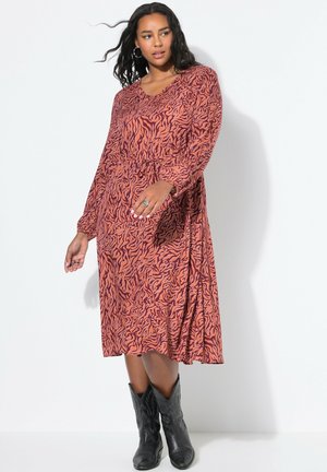 Vestido de manga larga en patrón abstracto naranja y negro, con escote en V, cintura ceñida y falda fluida. Lleva botas de cowboy negras.