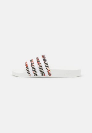 Tongs avec une semelle en caoutchouc blanc et des sangles en tissu à motifs rouge, noir et blanc. Comprend trois bandes verticales sur chaque sangle.