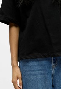 T-shirt en coton noir à manches courtes, coupe décontractée et ourlet au niveau des hanches. Associé à un jean en denim bleu, présentant une coupe droite.