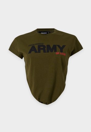 Дама, носеща маслинено зелена тениска "ARMY" с прорези и разкроени дънки с избелели участъци и износени платки, стояща с ръка в джоба.