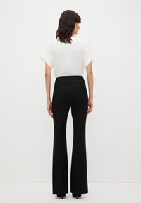 Zwarte flared trousers met een gladde textuur, met een gladde voorkant, achterzak en een maatwerk tailleband. Gecombineerd met een witte top.