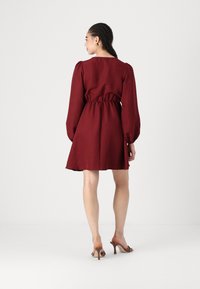 Rochie scurtă burgundă, cu mâneci lungi tip puff, talie strânsă și fustă evazată. Pur și simplu cu sandale cu toc maro. Textură netedă.