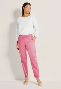 Witte top met lange mouwen gecombineerd met glanzende roze broek, voorzien van een losse pasvorm en opgerolde mouwen, aangevuld met naakte hoge hakken.