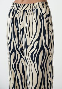 Beige broek met een marineblauwe zebra-streep patroon, met een elastische tailleband en zijzakken, gemaakt van een lichtgewicht stof.