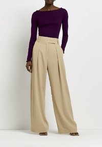 Bordowy top z długim rękawem i falbaną przy dekolcie, zestawiony z beżowymi spodniami o szerokich nogawkach, mającymi fałdy i wysoki stan. Gładka faktura tkaniny.