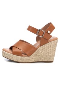 Sandalo wedge in pelle marrone con cinturini incrociati, fibbia alla caviglia e piattaforma in juta intrecciata. Texture liscia e forma della punta arrotondata.