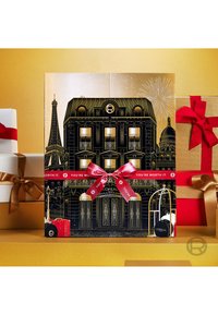 Schwarze Geschenkbox mit goldenen Akzenten zeigt ein illustriertes Pariser Gebäude, den Eiffelturm und ein rotes Band mit dem Text "DU BIST ES WERT."