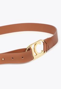 Brązowy skórzany pasek z metalową klamrą w złotym odcieniu, ozdobioną plecionym wzorem w kształcie "C". Gładka tekstura, regulowany rozmiar z otworami.